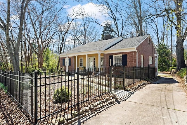 view of front of property featuring roof with shingles, driveway, a chimney, a fenced front yard, and brick siding