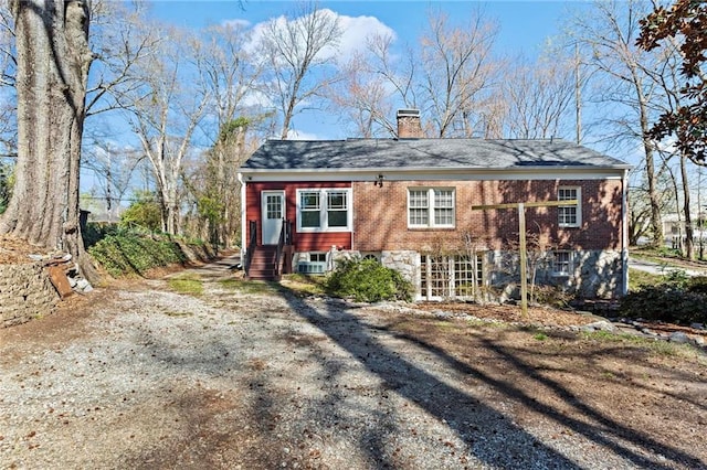 exterior space featuring driveway, brick siding, and a chimney