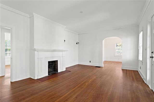 unfurnished living room featuring arched walkways, a fireplace with flush hearth, and crown molding