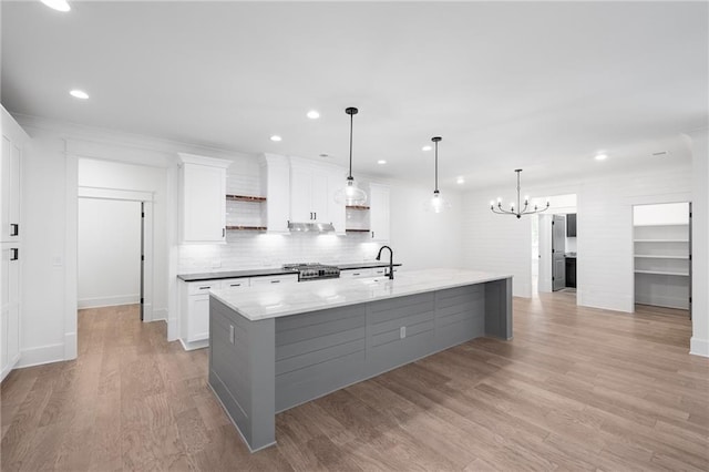 kitchen featuring a large island with sink, pendant lighting, light wood-type flooring, white cabinets, and light stone counters