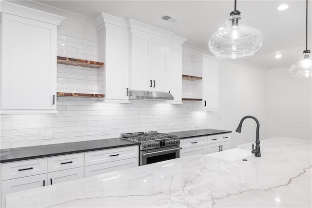 kitchen with sink, high end range, white cabinetry, decorative light fixtures, and dark stone counters