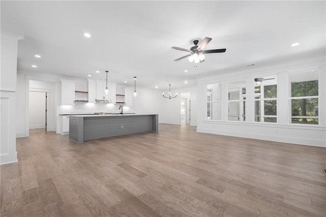 unfurnished living room featuring light hardwood / wood-style floors, ornamental molding, sink, and ceiling fan with notable chandelier