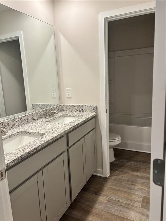 full bath with double vanity, wood finished floors, a sink, and toilet