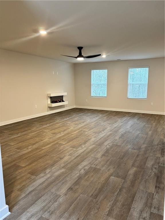 unfurnished living room featuring dark wood-style floors, a fireplace, baseboards, and a ceiling fan