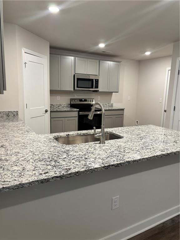 kitchen with light stone counters, recessed lighting, gray cabinetry, stainless steel appliances, and a sink