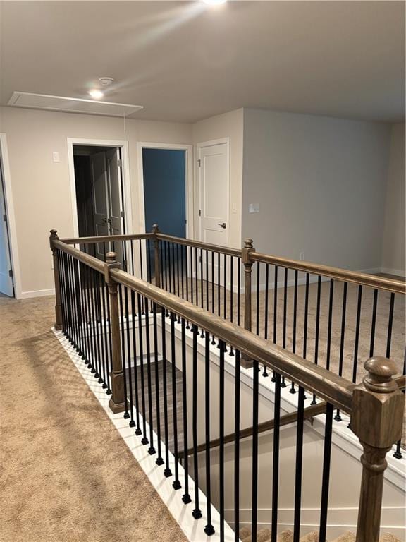 hallway featuring attic access, carpet, baseboards, and an upstairs landing