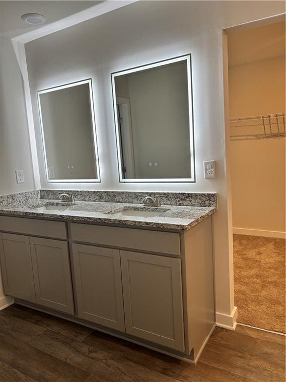 bathroom featuring double vanity, a spacious closet, a sink, wood finished floors, and baseboards