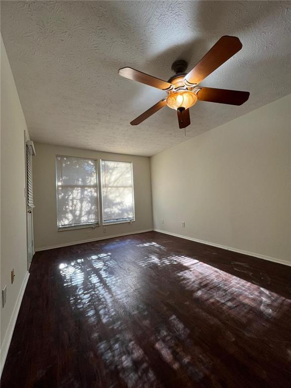 unfurnished room featuring ceiling fan, dark wood-type flooring, and a textured ceiling