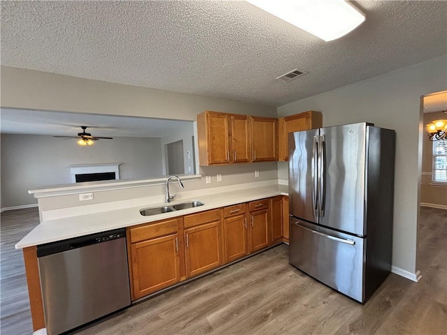 kitchen with ceiling fan with notable chandelier, sink, a textured ceiling, light hardwood / wood-style floors, and stainless steel appliances