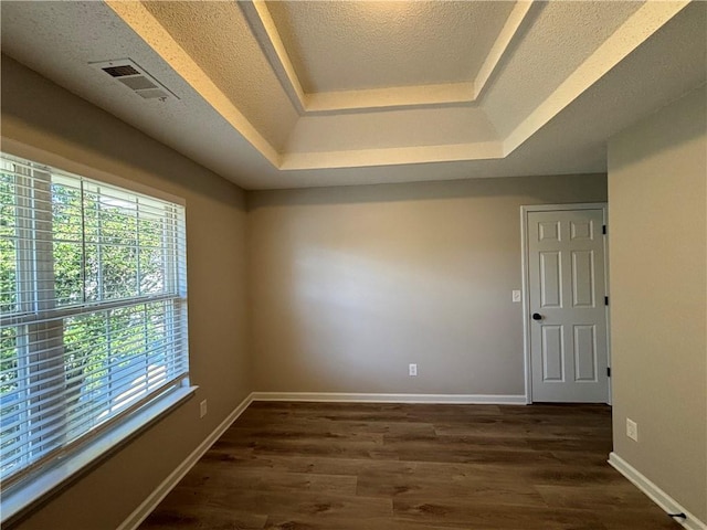 unfurnished room with a healthy amount of sunlight, dark hardwood / wood-style flooring, a textured ceiling, and a tray ceiling