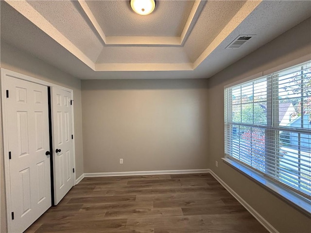 unfurnished bedroom with a raised ceiling, dark hardwood / wood-style flooring, and a textured ceiling