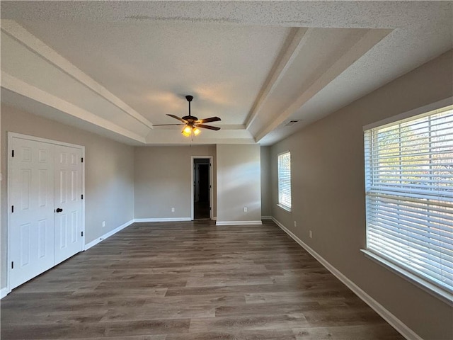 unfurnished room with a tray ceiling, ceiling fan, dark wood-type flooring, and a textured ceiling