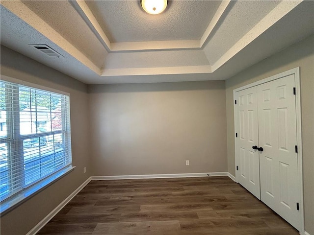 interior space with a textured ceiling, a closet, dark wood-type flooring, and a tray ceiling