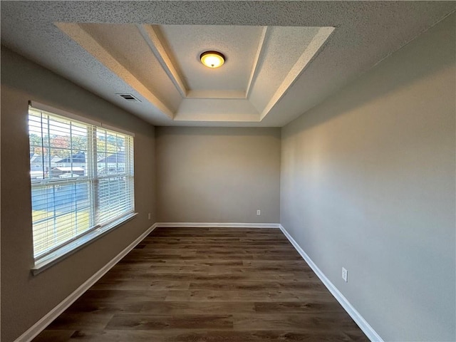 empty room featuring a tray ceiling, dark wood-type flooring, and a textured ceiling