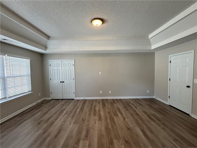 unfurnished bedroom featuring a textured ceiling, dark hardwood / wood-style flooring, and a tray ceiling