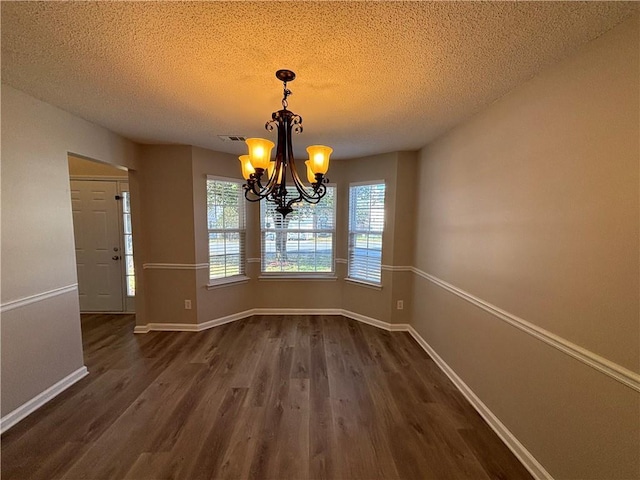 unfurnished dining area with dark hardwood / wood-style flooring, a textured ceiling, and a notable chandelier