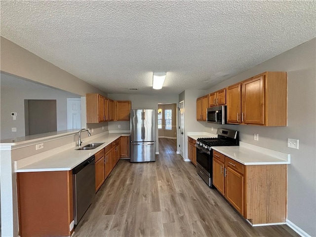 kitchen featuring sink, light hardwood / wood-style flooring, a textured ceiling, appliances with stainless steel finishes, and kitchen peninsula