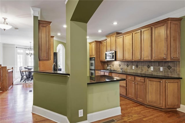 1605 Pavillion Ridge Dr SE, Smyrna, GA 30080 - kitchen featuring appliances with stainless steel finishes, dark countertops, brown cabinetry, decorative backsplash, and ornamental molding