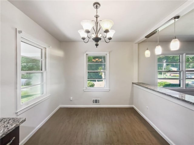 unfurnished dining area featuring dark wood-style floors, visible vents, baseboards, and an inviting chandelier