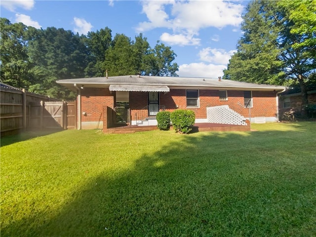 back of property with brick siding, a lawn, and fence