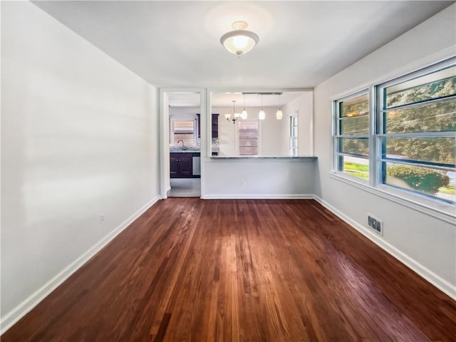 spare room with an inviting chandelier, baseboards, visible vents, and dark wood-type flooring