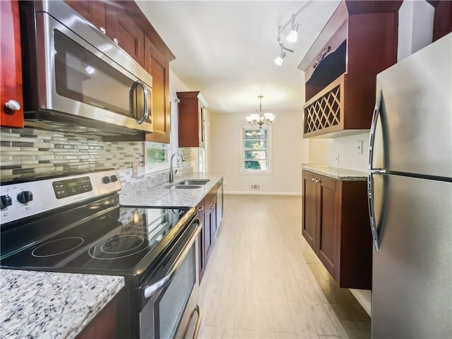 kitchen featuring a sink, appliances with stainless steel finishes, backsplash, light stone countertops, and an inviting chandelier