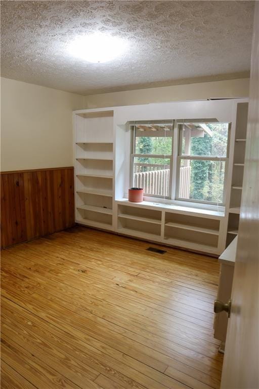 empty room with a textured ceiling, wainscoting, light wood-type flooring, and wooden walls