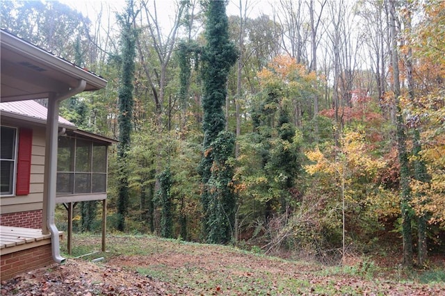view of yard featuring a sunroom and a view of trees