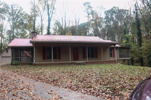 view of front of home with a sunroom, a chimney, metal roof, a garage, and brick siding