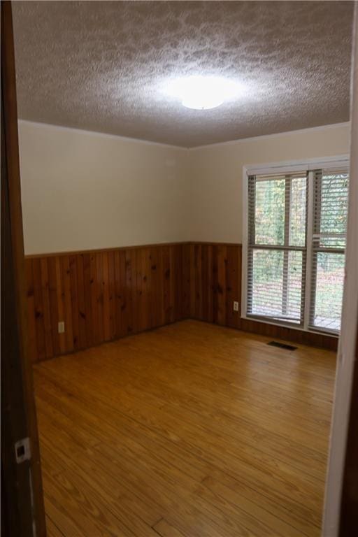 unfurnished room featuring a textured ceiling, wood finished floors, wood walls, and a wainscoted wall