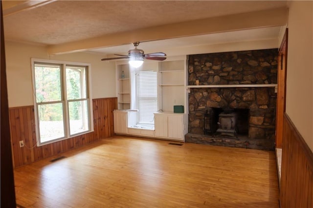 unfurnished living room with a wainscoted wall, light wood finished floors, beam ceiling, ceiling fan, and wood walls