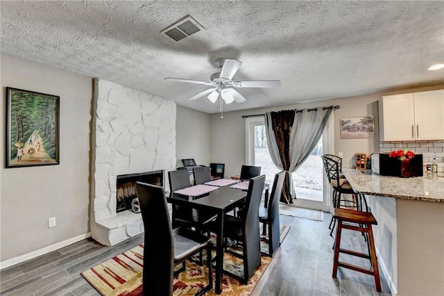 dining space with a stone fireplace, dark hardwood / wood-style floors, a textured ceiling, and ceiling fan