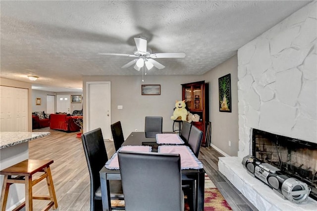 dining area featuring hardwood / wood-style floors, a stone fireplace, and a textured ceiling