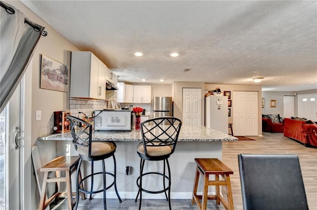 kitchen with white cabinetry, stainless steel fridge, a kitchen breakfast bar, white refrigerator, and light stone counters