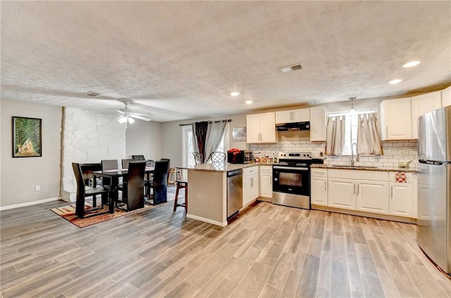 kitchen featuring light stone countertops, appliances with stainless steel finishes, backsplash, and kitchen peninsula