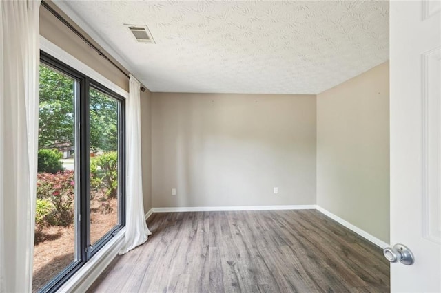 unfurnished room featuring baseboards, a textured ceiling, wood finished floors, and visible vents