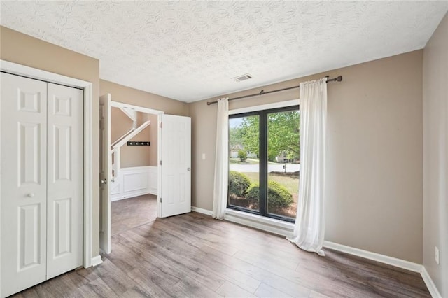 unfurnished bedroom featuring a textured ceiling, a closet, wood finished floors, and visible vents
