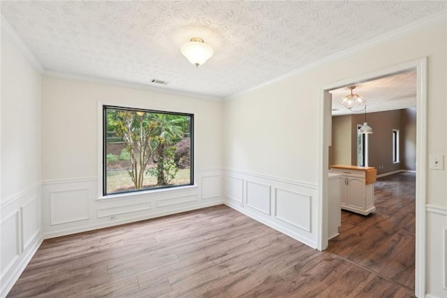 unfurnished room featuring visible vents, wainscoting, wood finished floors, a textured ceiling, and a notable chandelier