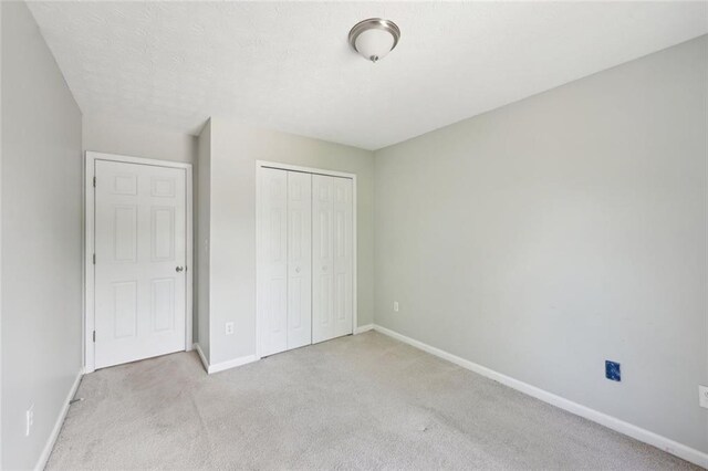 unfurnished bedroom featuring baseboards, light carpet, and a closet