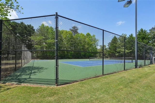 view of tennis court with a lawn and fence