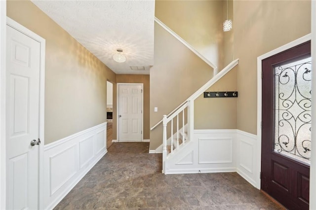 foyer featuring stone finish flooring, wainscoting, a decorative wall, and stairway