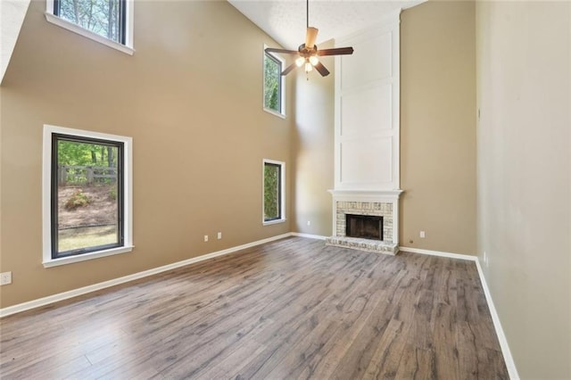 unfurnished living room featuring wood finished floors, a ceiling fan, a healthy amount of sunlight, and a towering ceiling