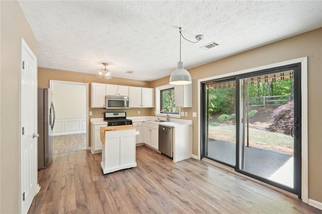 kitchen featuring appliances with stainless steel finishes, a sink, light wood-style flooring, a center island, and visible vents