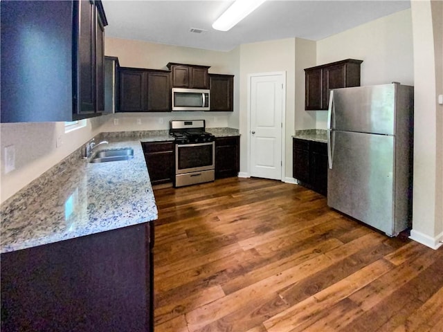 kitchen with sink, dark hardwood / wood-style floors, light stone countertops, appliances with stainless steel finishes, and dark brown cabinetry