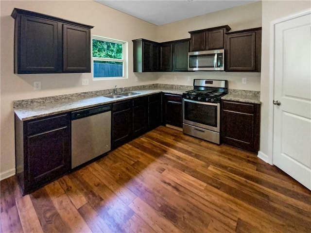 kitchen with appliances with stainless steel finishes, dark hardwood / wood-style floors, dark brown cabinets, and sink