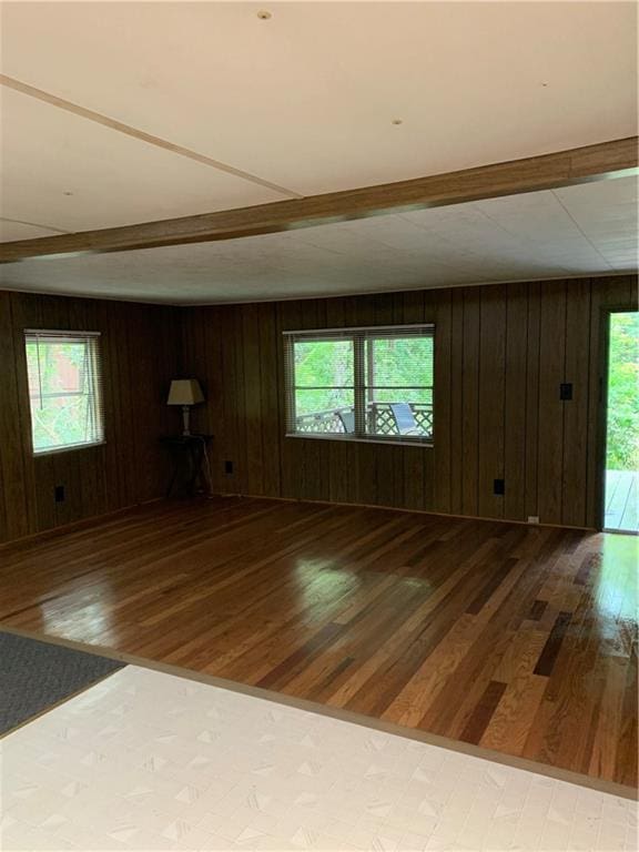 unfurnished living room featuring beam ceiling, wood-type flooring, and wood walls