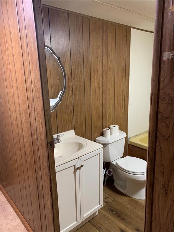 bathroom featuring toilet, vanity, wood walls, hardwood / wood-style flooring, and a bathtub