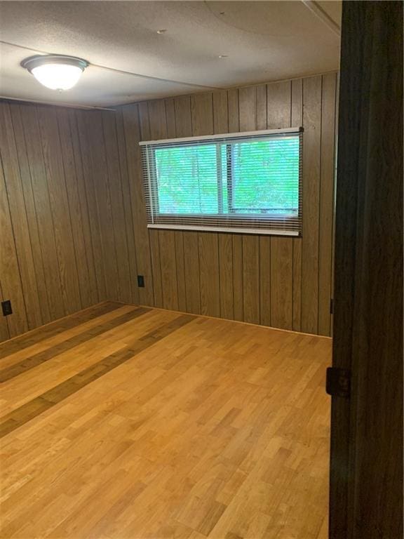 unfurnished room with light wood-type flooring and wooden walls