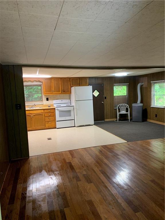 kitchen featuring dark hardwood / wood-style floors, a healthy amount of sunlight, wood walls, and white appliances