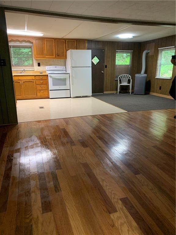 kitchen featuring a wealth of natural light, dark wood-type flooring, wood walls, and white appliances